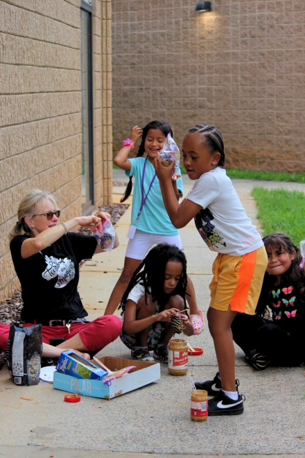 Students and an adult gather outside for a hands-on activity using jars, cups and other materials.