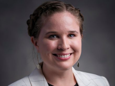 A headshot of Olivia Cox on a gray background