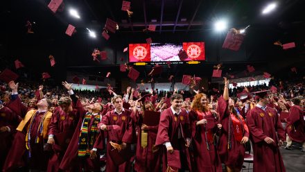 graduates throw caps in the air at Commencement
