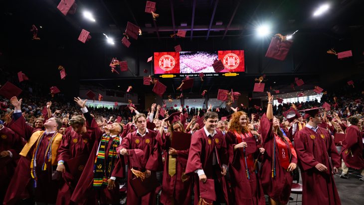 graduates throw caps in the air at Commencement