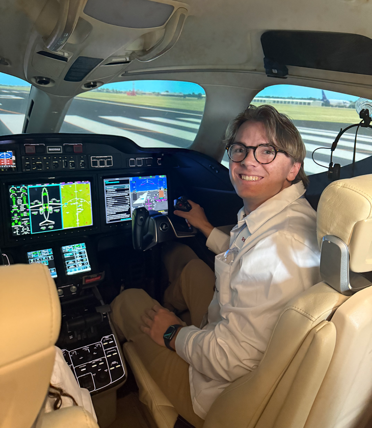 Oliver Keicher smiles from the pilot’s seat inside a HondaJet cockpit, surrounded by illuminated flight controls and display screens.