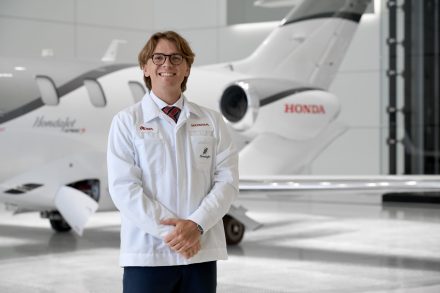 Oliver Keicher stands in a white Honda work coat in front of a HondaJet inside an aircraft hangar.