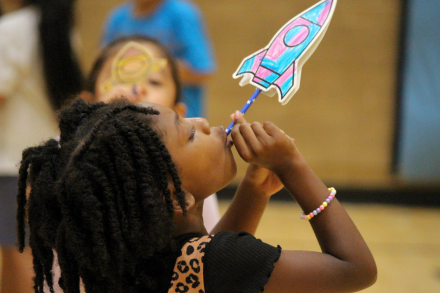 A student holds up and looks closely at a colorful paper rocket during a classroom activity.