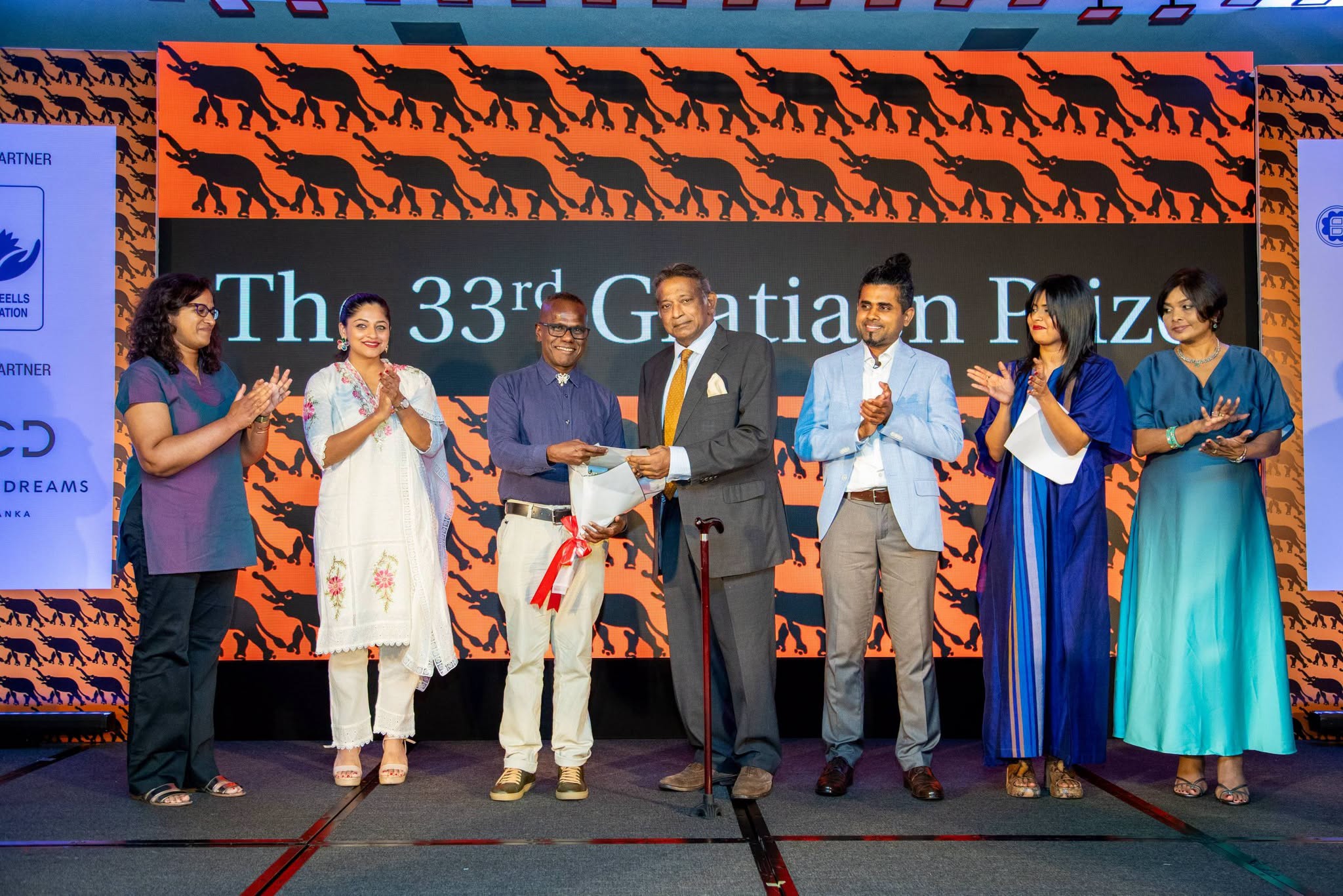 Seven people stand onstage applauding during an awards presentation at the 33rd Gratiaen Prize