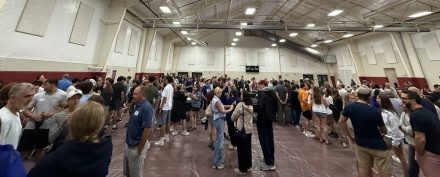 Students, families and staff gather inside a large gymnasium during a crowded campus event.
