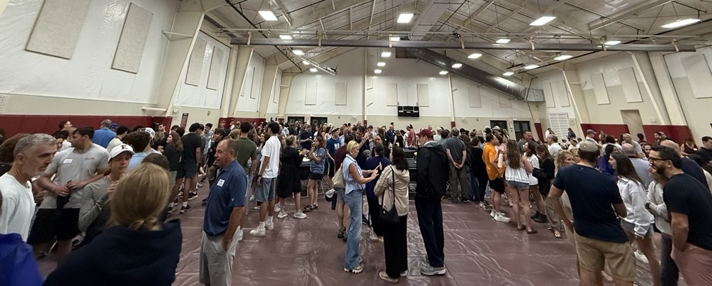 Students, families and staff gather inside a large gymnasium during a crowded campus event.