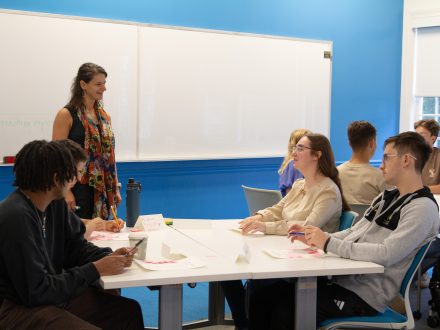 Professor Olivia Choplin speaking to a table with four students.