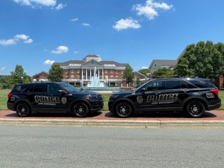 Two �������޹�����Ʒ Police SUVs are parked nose to nose in front of Young Commons, with the fountain spraying beneath a bright blue sky.