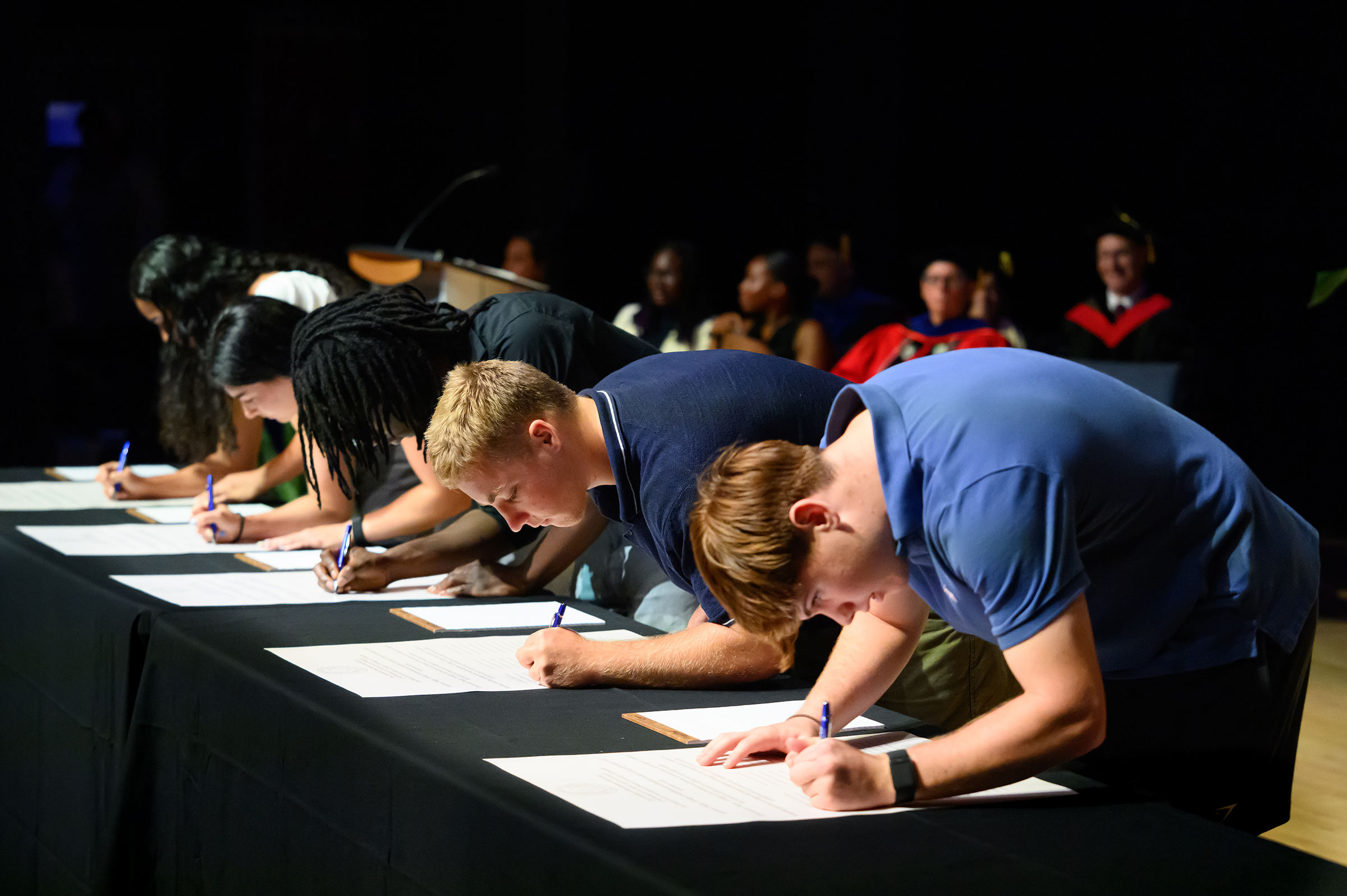 Five students hunch over a table to sign the Queens Honor Code.