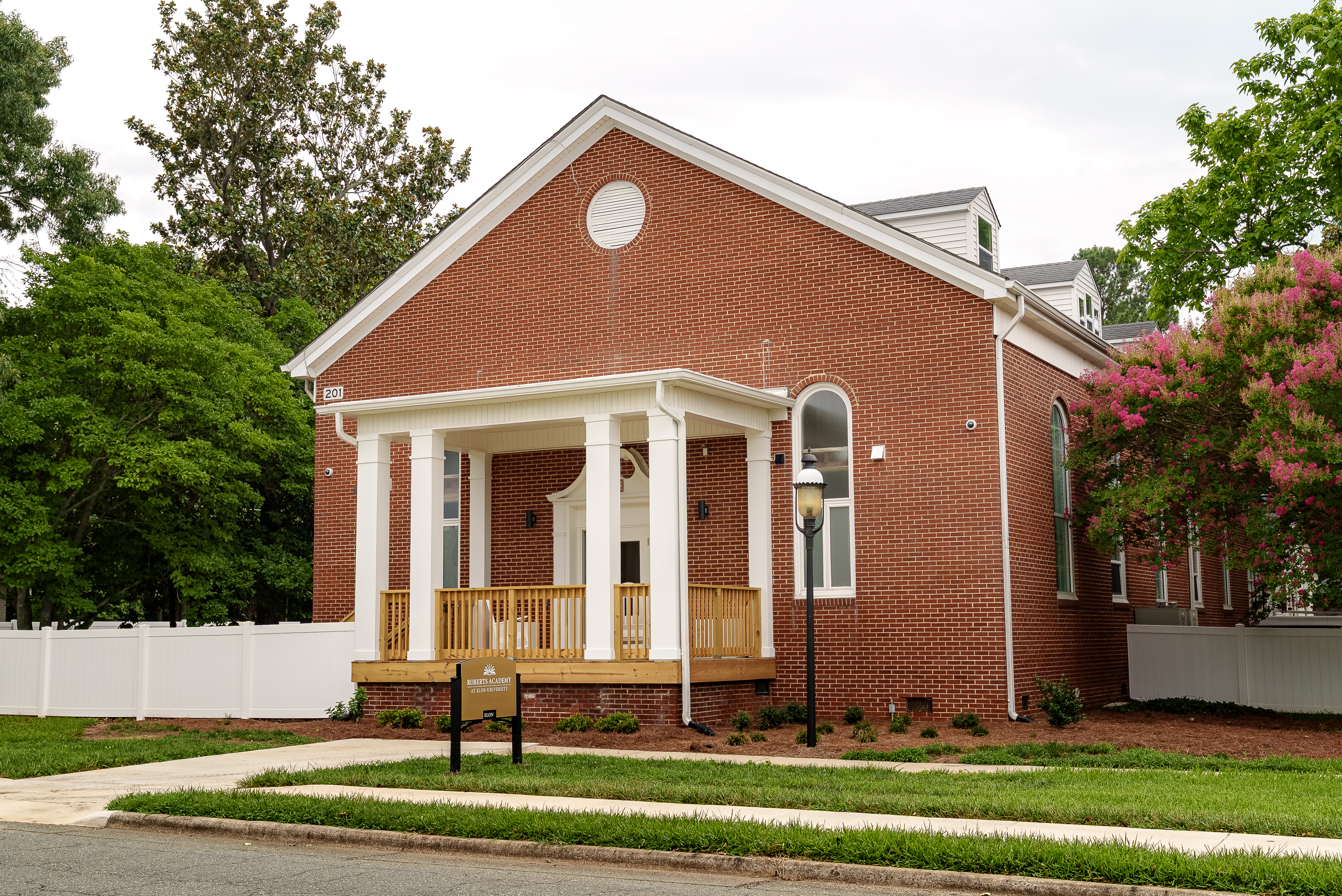 The renovated Trollinger House features a restored brick exterior, white columns, a new front porch and landscaping. A sign identifies it as the temporary home of Roberts Academy at 51������.