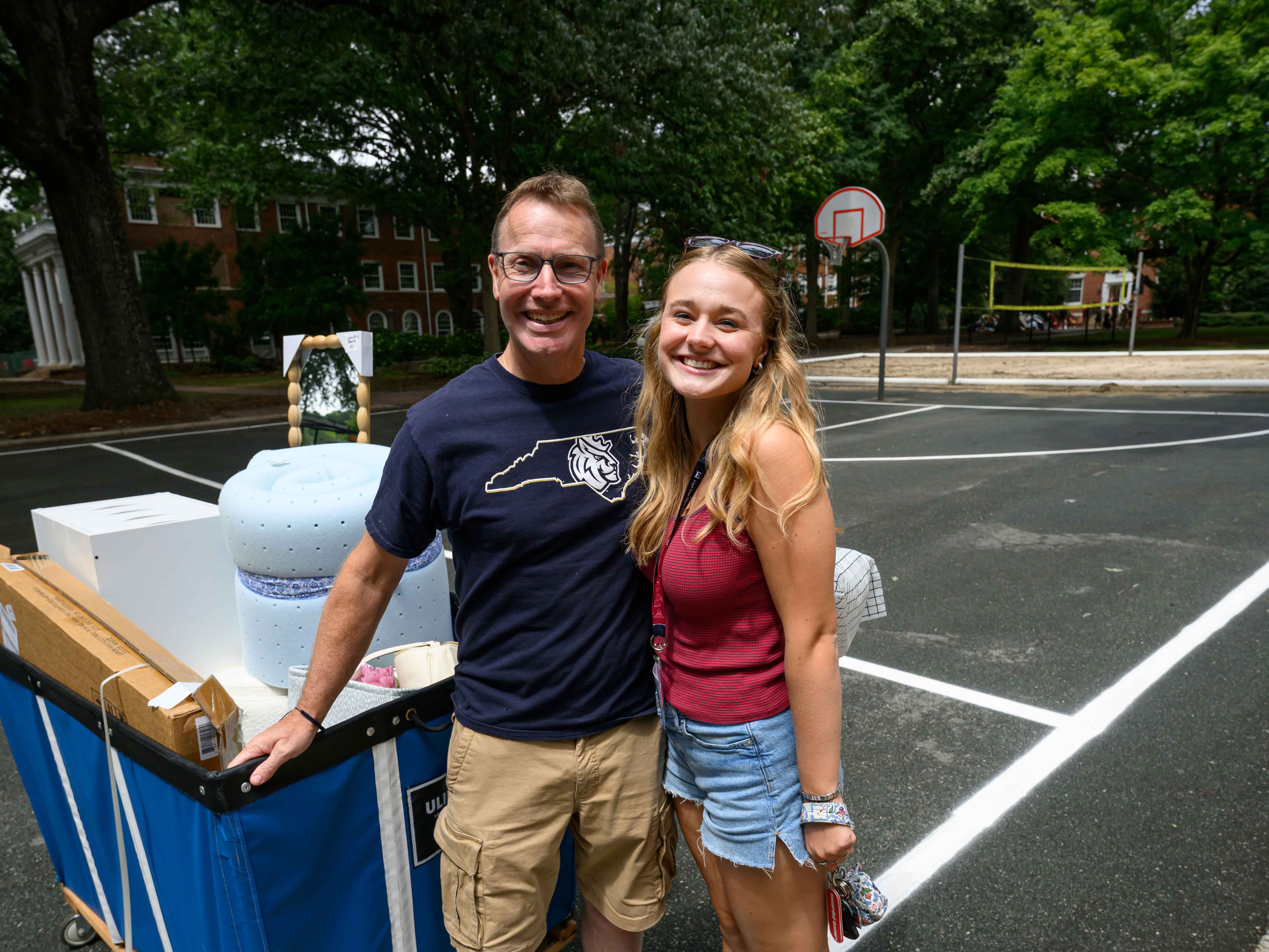 man with navy blue Queens University teeshirt on stands with girl with long blond hair wearing shorts and a maroon tank top.