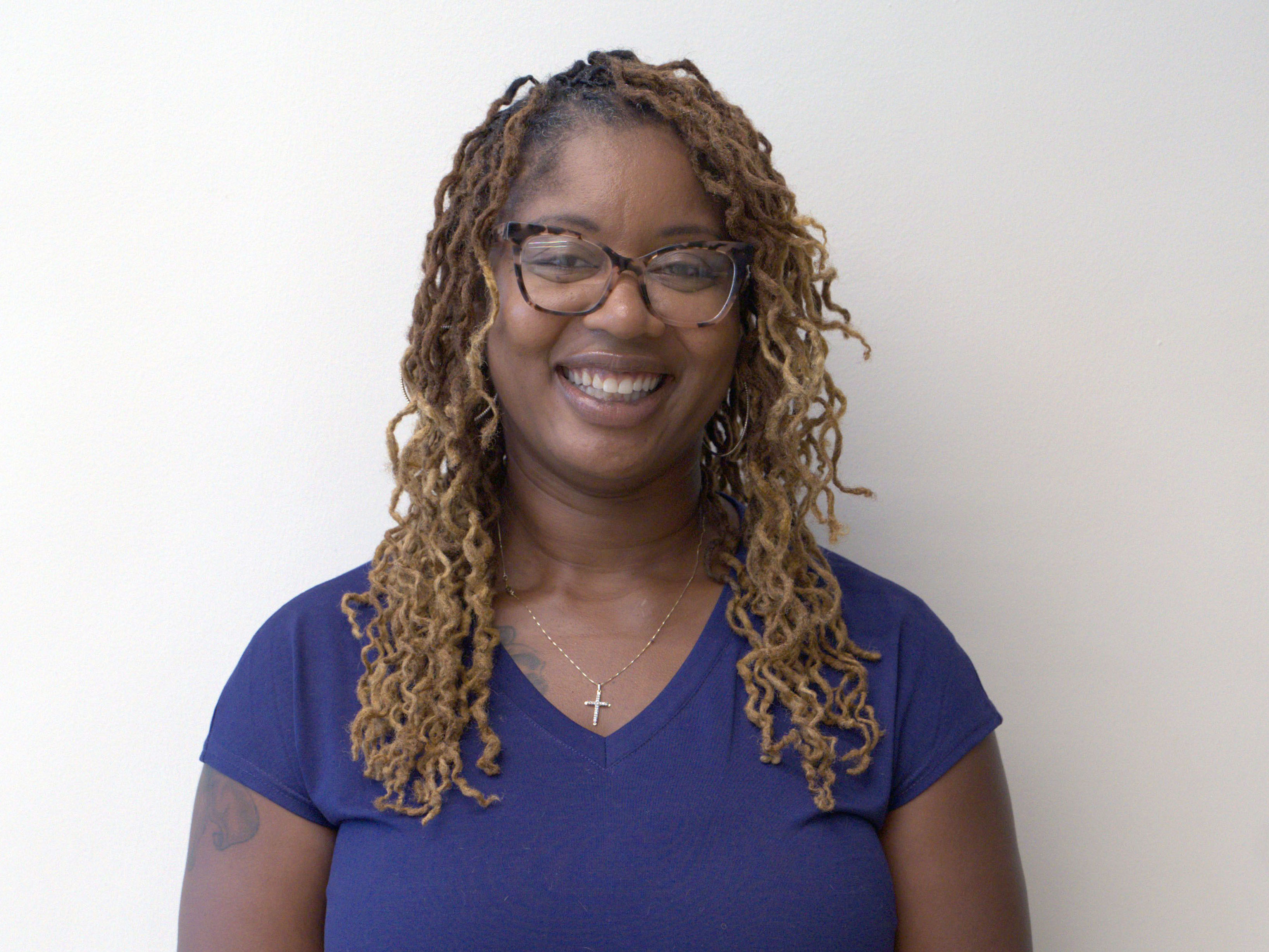 Headshot of a woman with glasses, blonde curly hair and purple short sleeve shirt. 