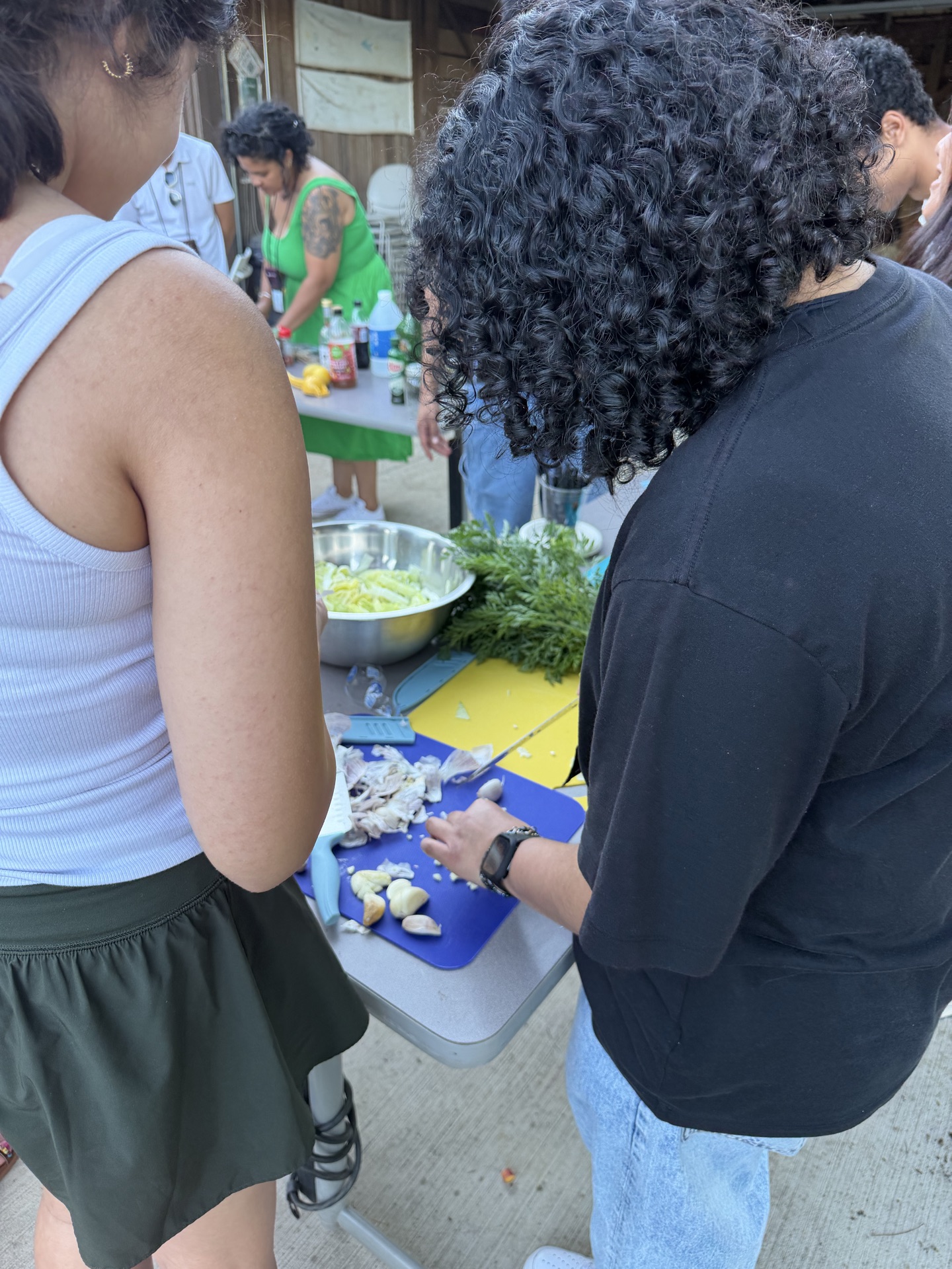 Two Elon Academy Scholars use a knife to mince garlic in an outdoor learning space. 