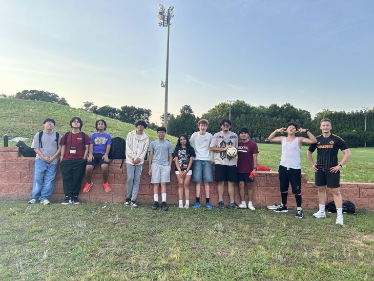 A group of Elon Academy Scholars line up for a picture with their soccer instructor in front of Elon University's Intramural fields.