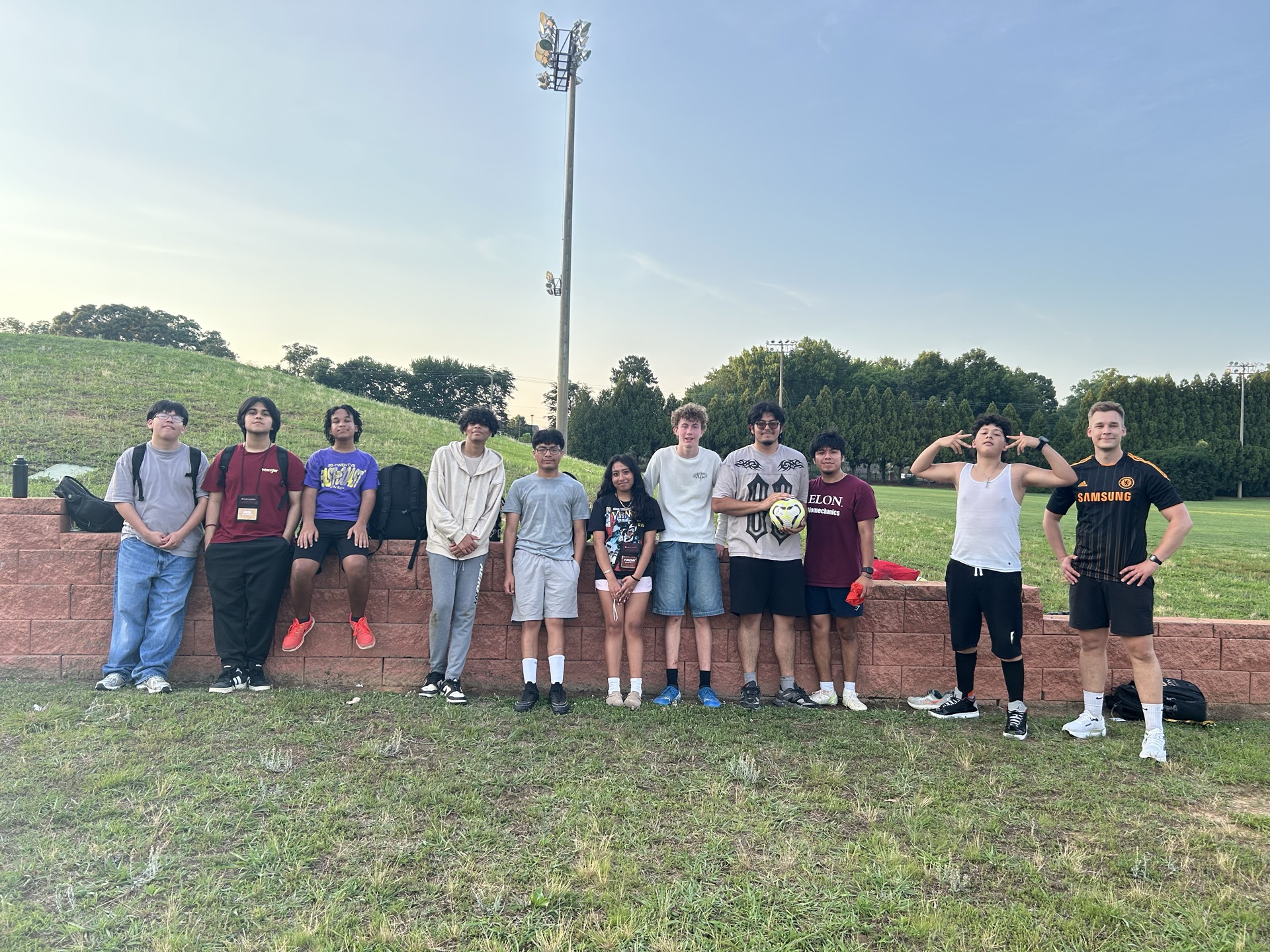A group of Elon Academy Scholars line up for a picture with their soccer instructor in front of Elon University's Intramural fields.