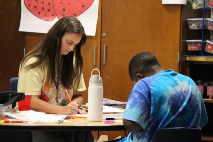 A teacher works with a student on an assignment at a classroom table.