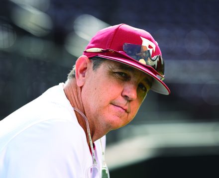 Elon baseball head coach Mike Kennedy wears an Elon baseball cap and looks toward the camera.