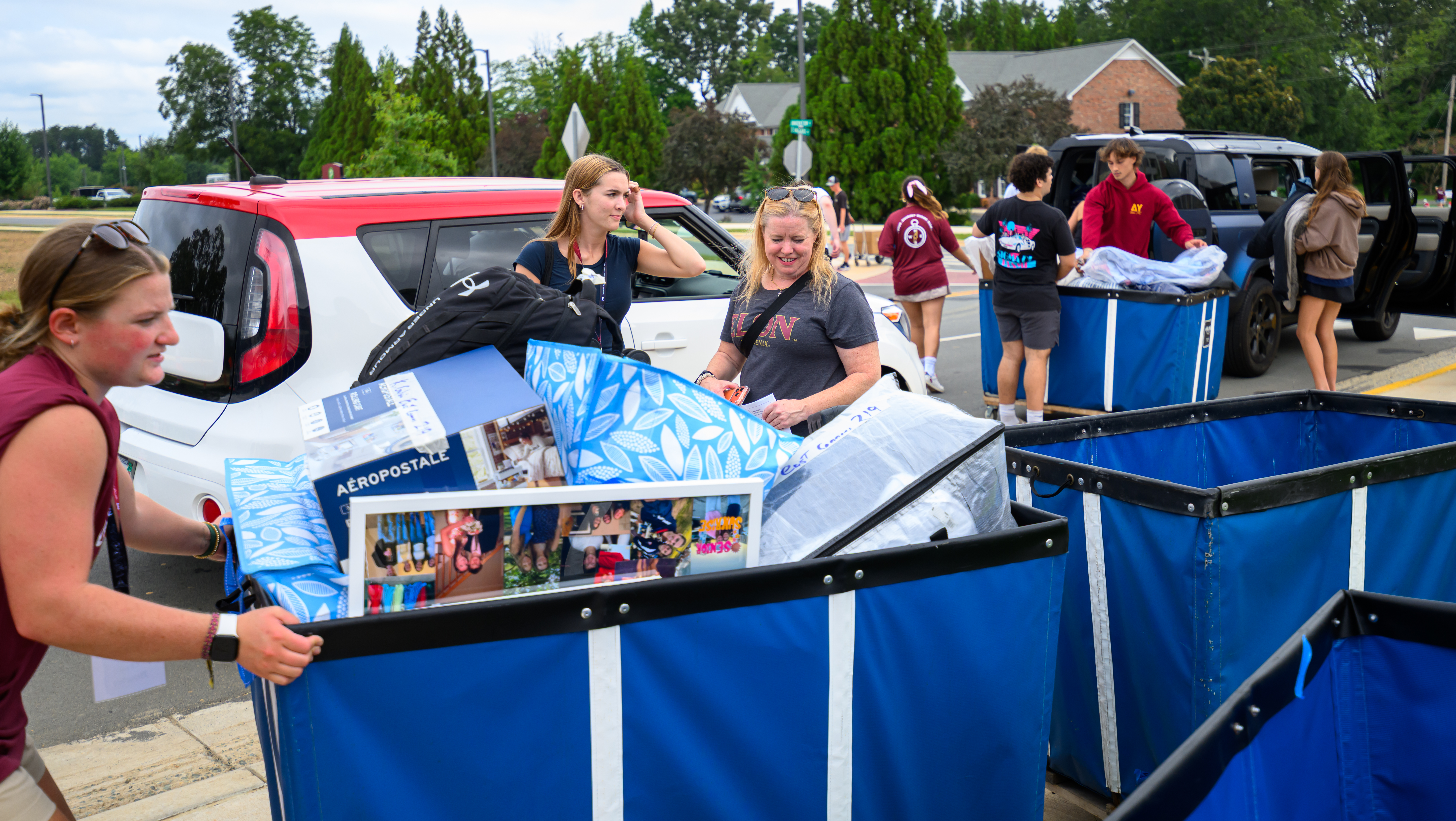 Students, families and volunteers unload cars and push large blue carts filled with belongings during Elon’s Move-In Day.