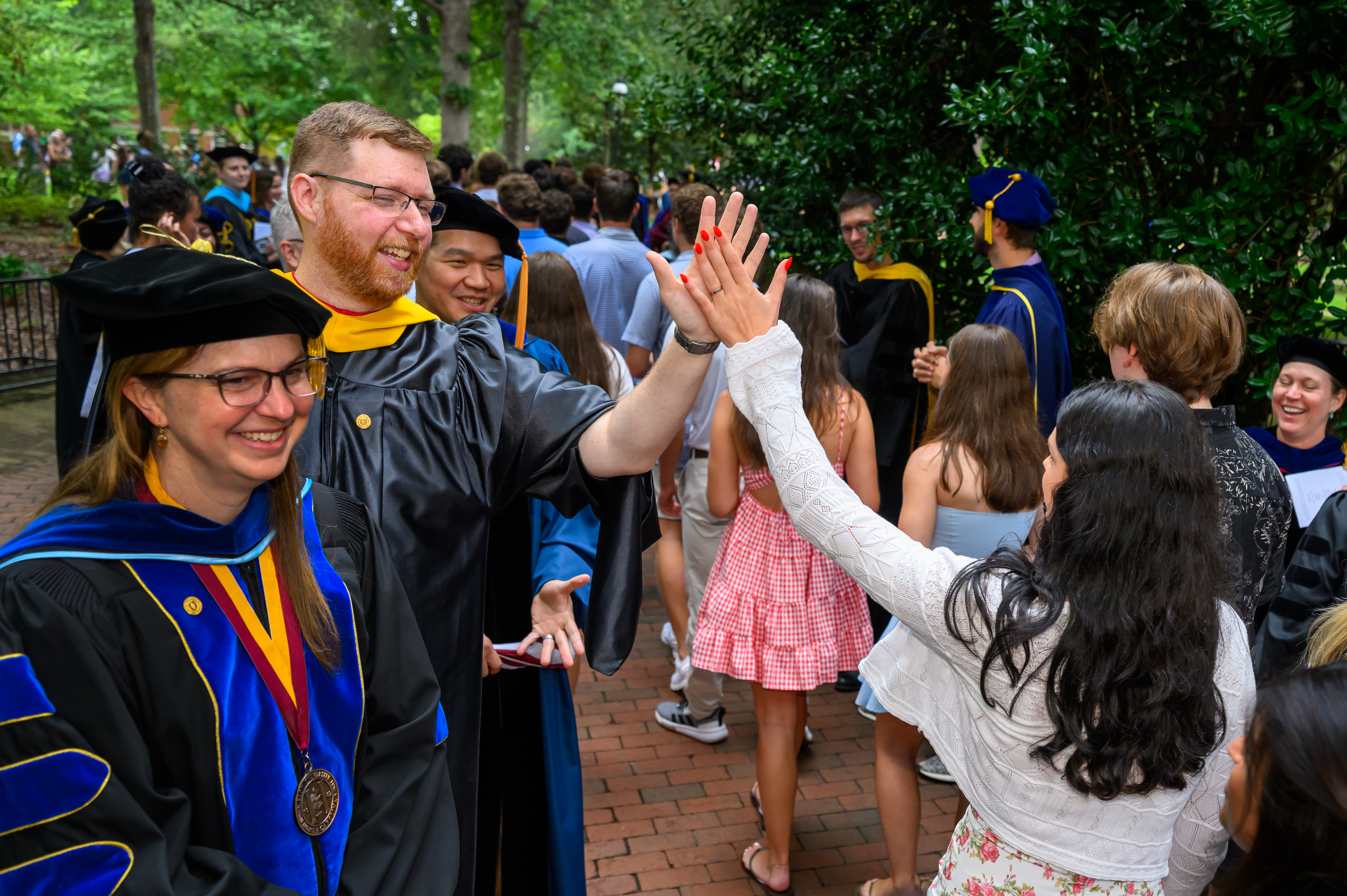 An Elon faculty member in academic regalia high-fives a student following New Student Convocation.