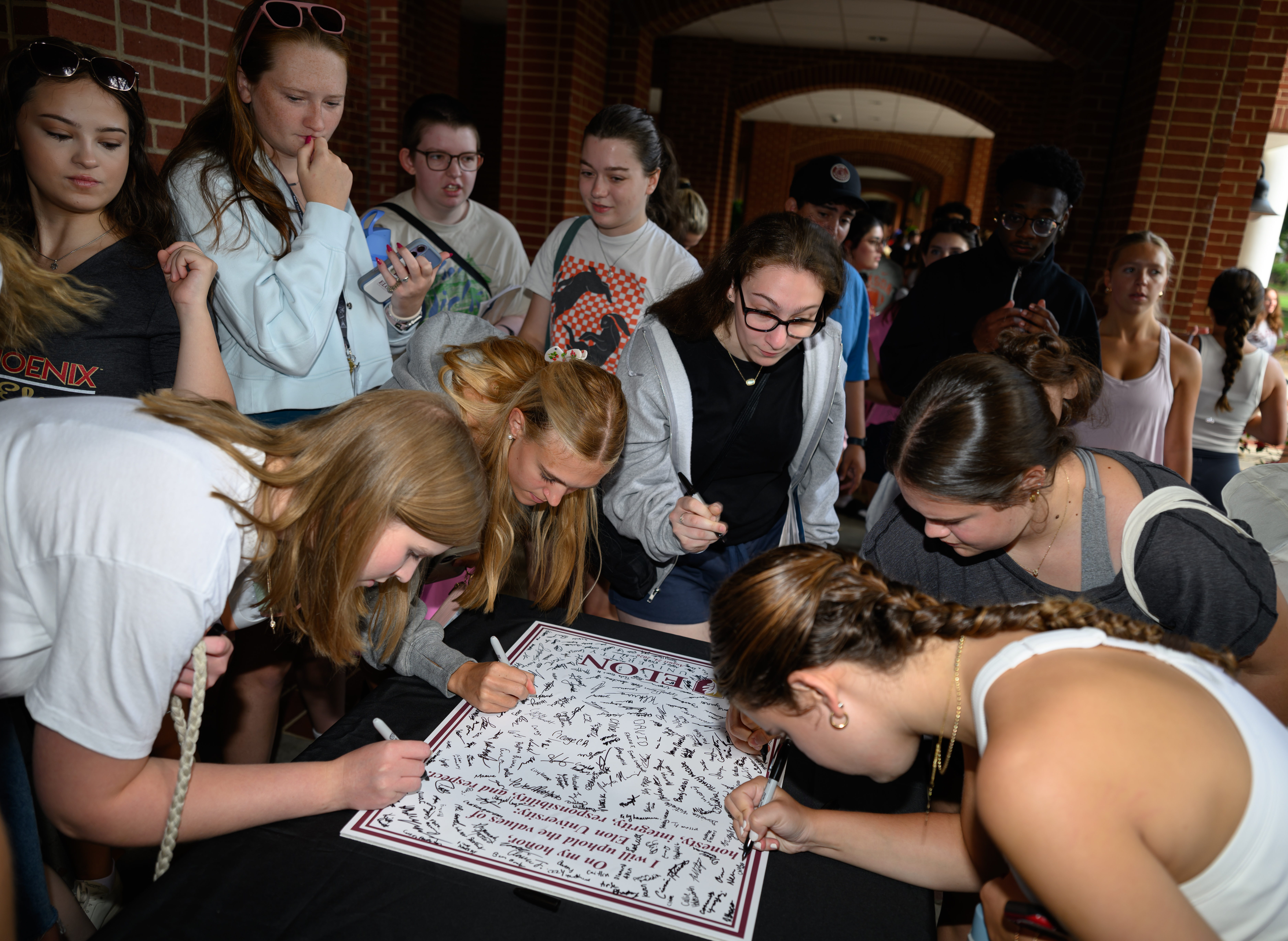 Students gather around a table to sign an Elon Honor Code poster during the Call to Honor ceremony.