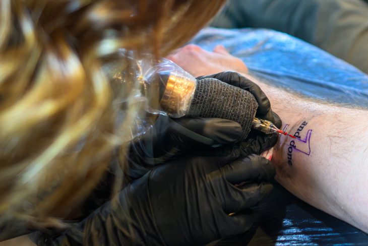 Closeup of hands holding a tattoo needle onto skin.