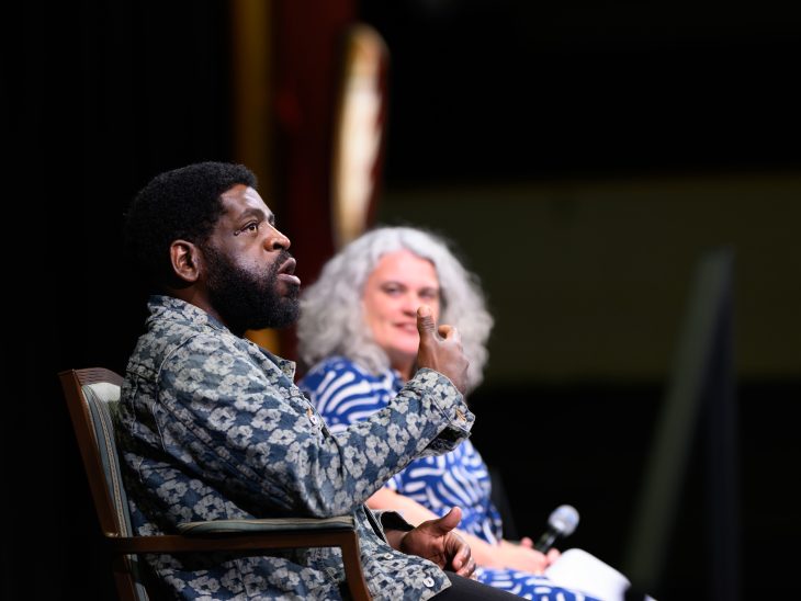     A guest speaker gestures while speaking onstage as the moderator listens beside him.