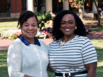 Two women in white blouses stand next to each other smiling.