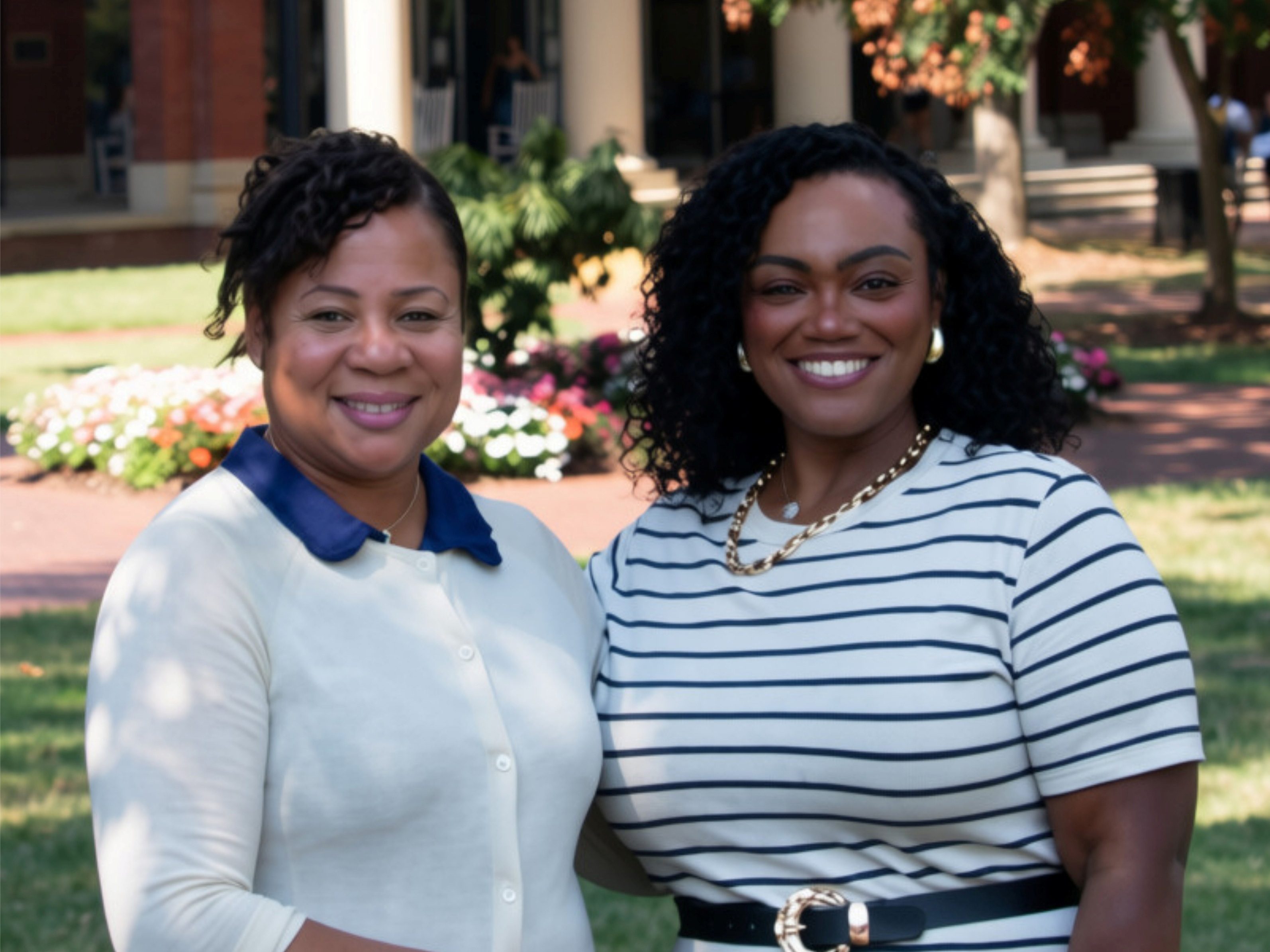 Two women in white blouses stand next to each other smiling.