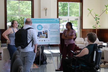 Students and faculty discuss a research poster during a presentation in a campus gathering space.