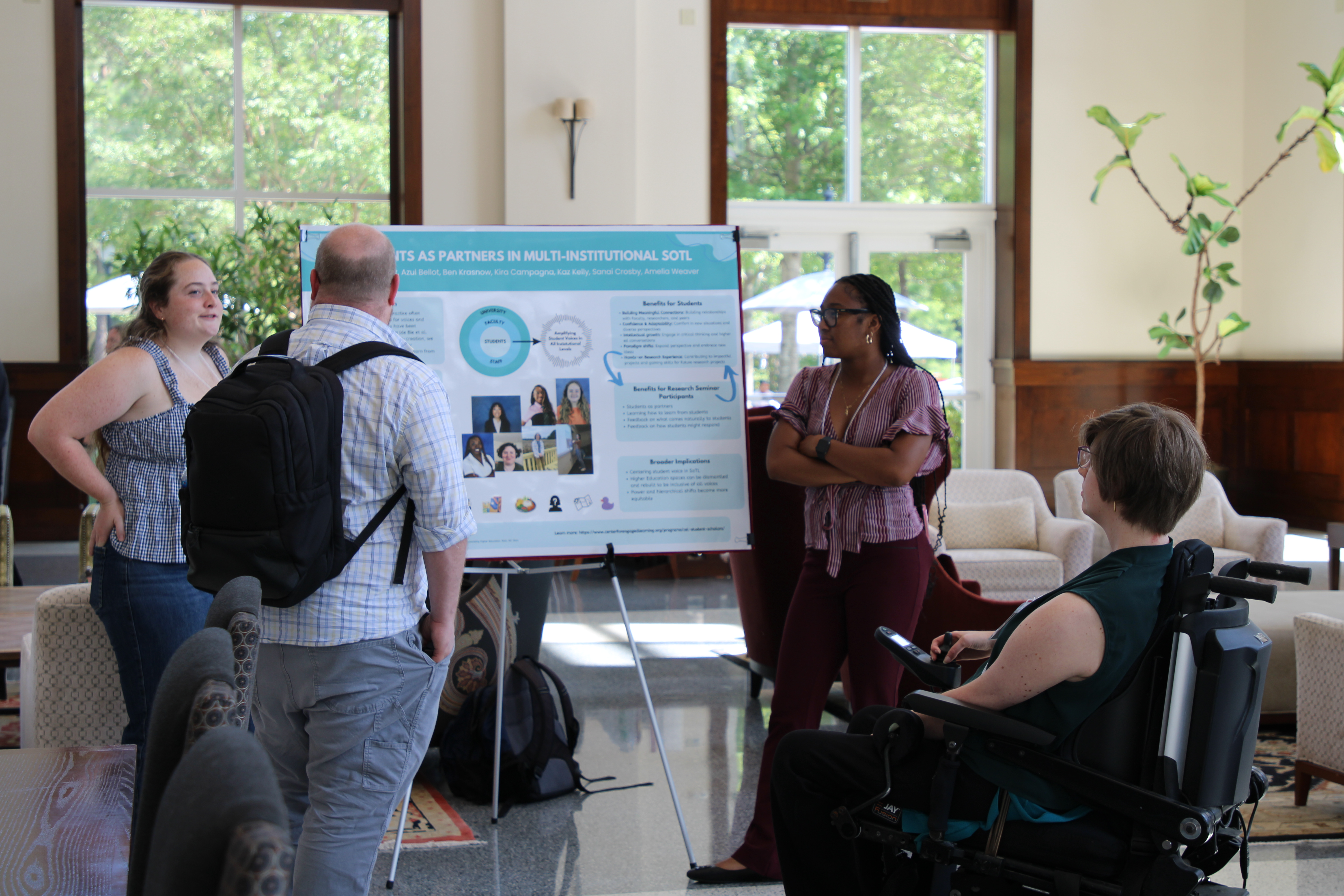 Students and faculty discuss a research poster during a presentation in a campus gathering space.