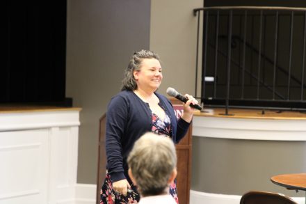 A woman stands with a microphone in hand smiling