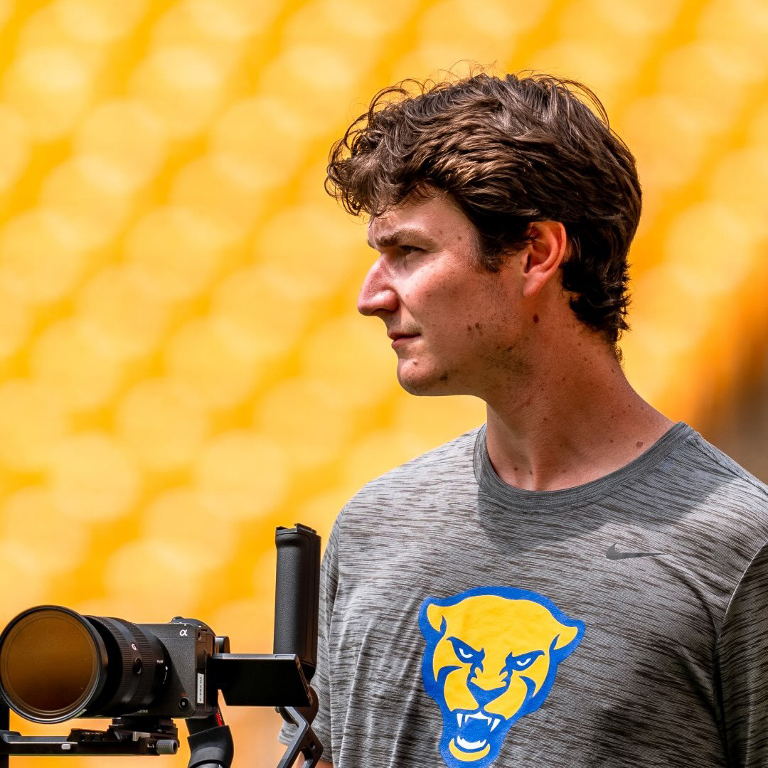 Cap Henneman stands before yellow grandstands at a Pitt football event.