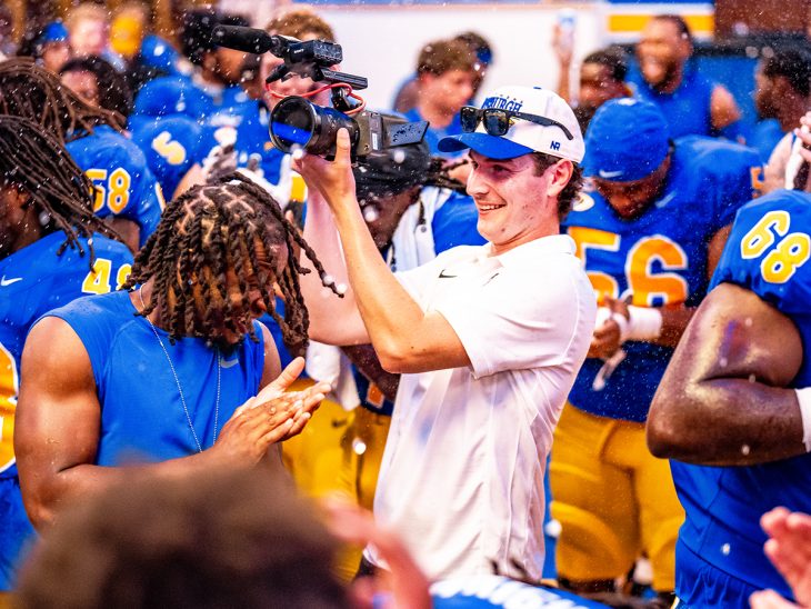 Elon alumnus Cap Henneman stands in a crowded blue and yellow lockerroom.