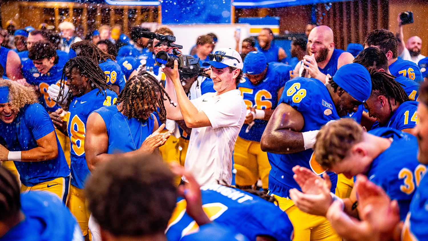 Elon alumnus Cap Henneman stands in a crowded blue and yellow lockerroom.