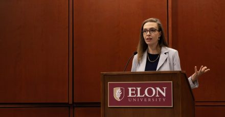 Photo of woman in a blazer standing a podium speaking.