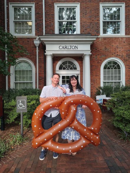 Two German Studies faculty members standing holding an inflatable pretzel.
