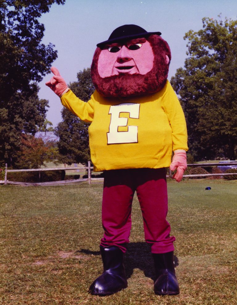 Elon’s Fighting Christian mascot, wearing a yellow shirt with a large “E,” poses outdoors in 1978.