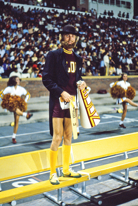 Elon’s Fighting Christian mascot stands on the bleachers holding a megaphone during a football game in the 1980s.