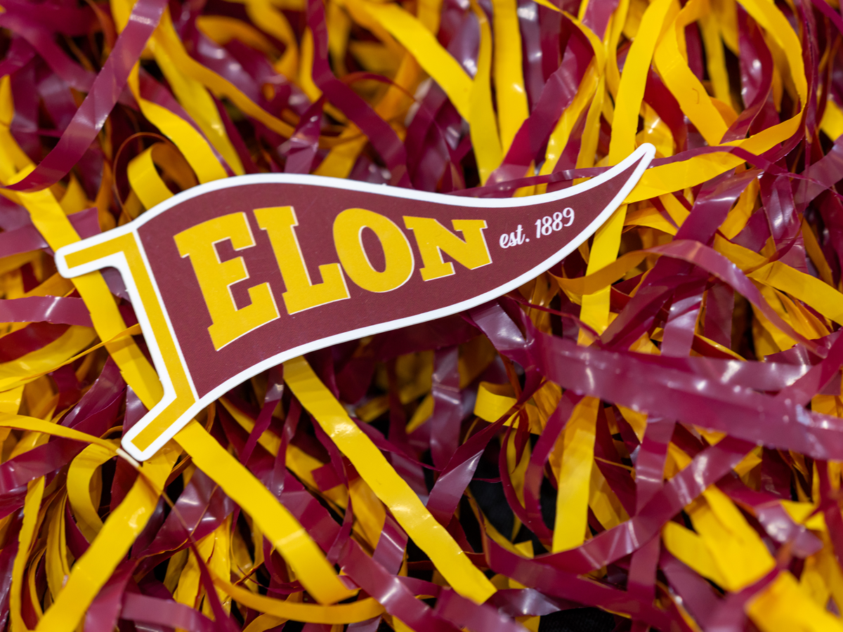 Elon, est. 1889' pennant resting on maroon and gold shredded paper, likely for Homecoming.