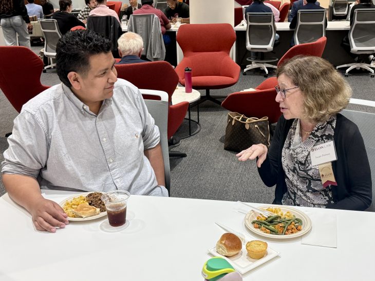 two people seated at a table, speaking over a meal.