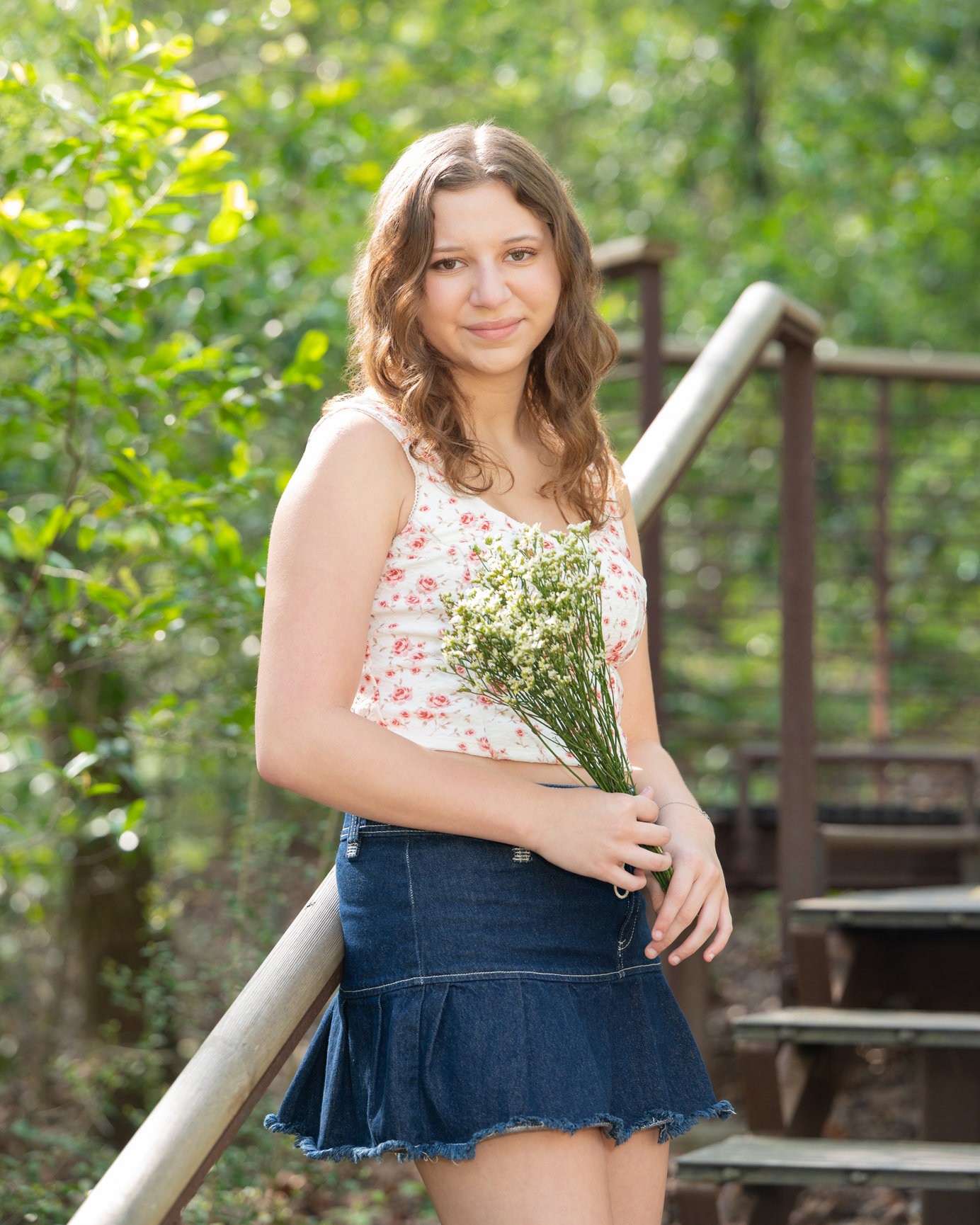 A young woman stands in a skirt and sleeveless shirt on wooden steps outside