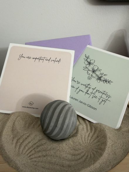 Two encouragement cards, 'You are important and valued!' and 'You're worthy of greatness, even if you don't see it yet,' resting on a mini zen garden