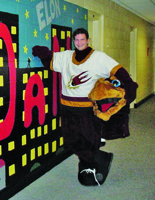 A student poses in a partially removed Phoenix mascot costume, holding the mascot head beside him.