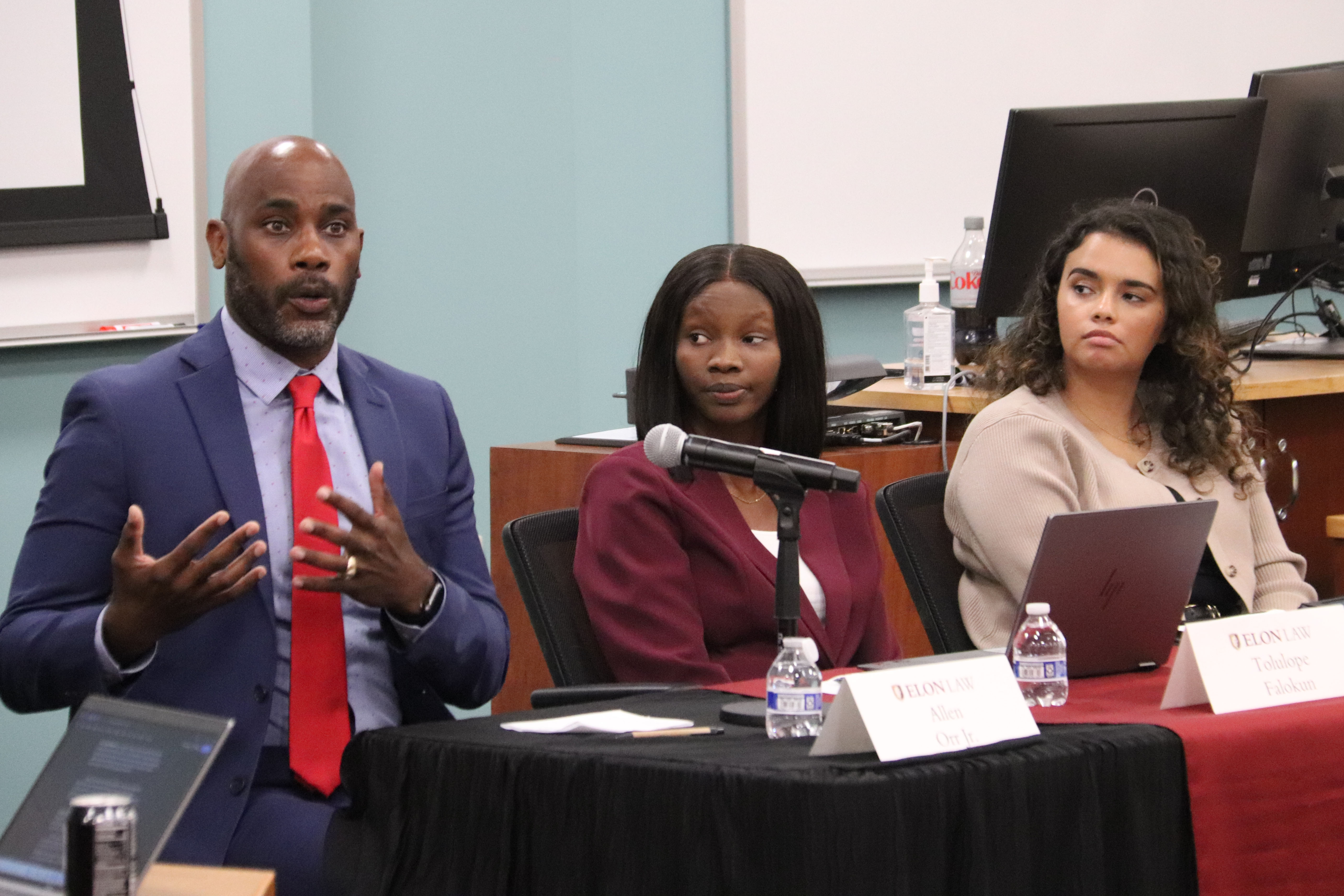 A photo of From left: Allen Orr Jr., Founder and Principal Attorney of Orr Immigration Law Firm; Tolulope Falokun, Assistant Professor of Law at the University of Detroit Mercy School of Law; and Jordin Dickerson, Assistant Professor of Political Science and Public Administration at the University of North Carolina at Pembroke, at the Elon Law Review's 2026 symposium. Orr, in a blue suit and red tie, is addressing the audience in this photo.