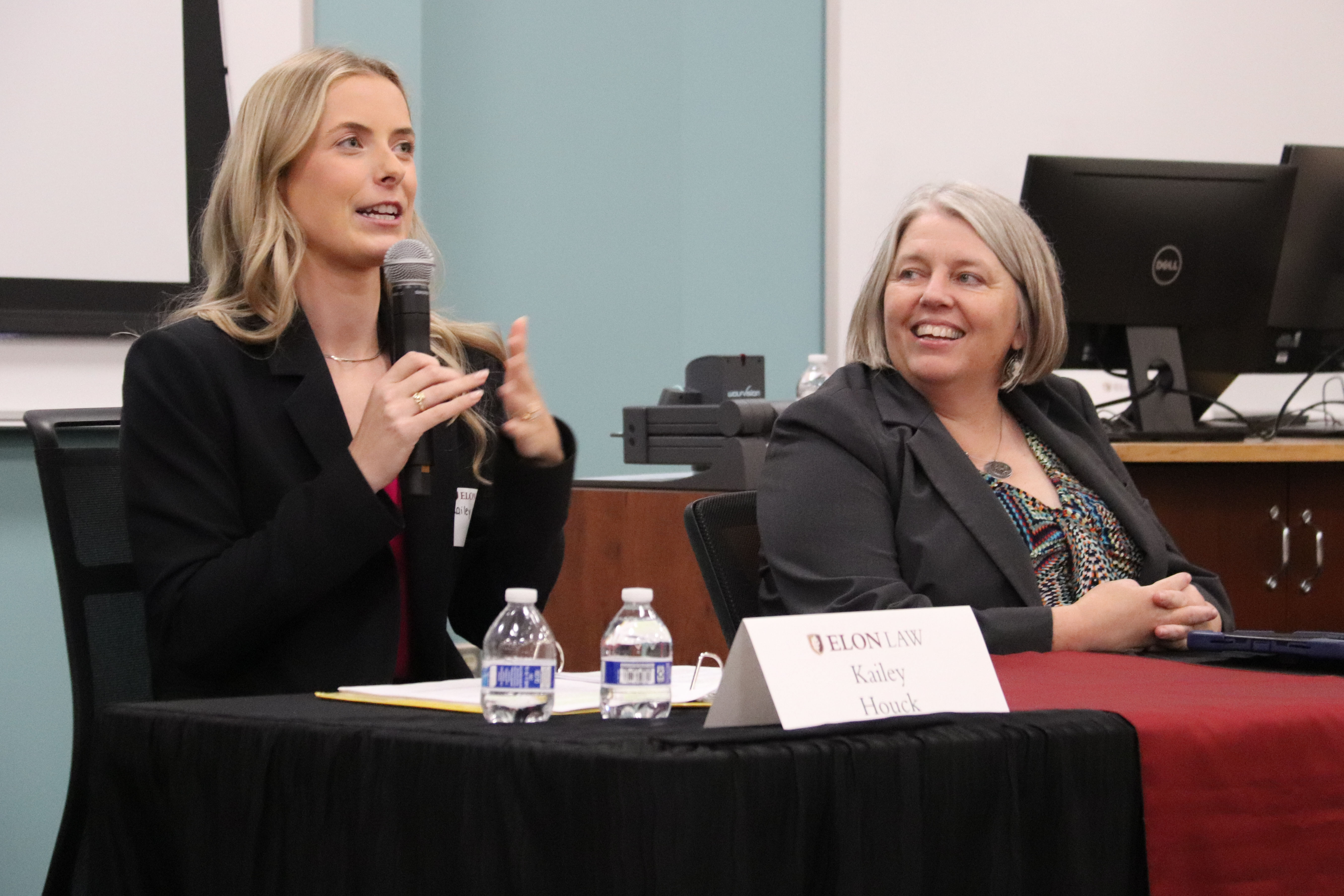 A photo of Kailey Houck, Judicial Law Clerk for Justice Melissa Hart and Justice Susan Blanco of the Colorado State Supreme Court, holding a microphone and addressing an audience at the Elon Law Review's 2026 symposium. and Maria Rosales, Executive Director of FaithAction International.