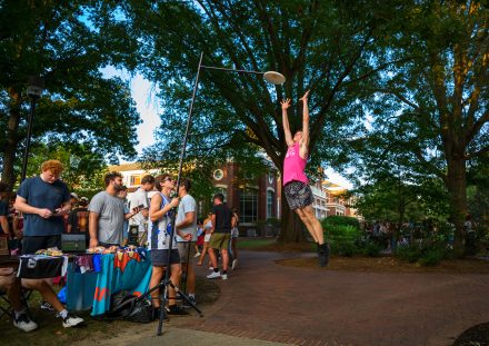 A student leaps to catch a flying disc during the Fall Organization Fair as students gather around tables on Young Commons.