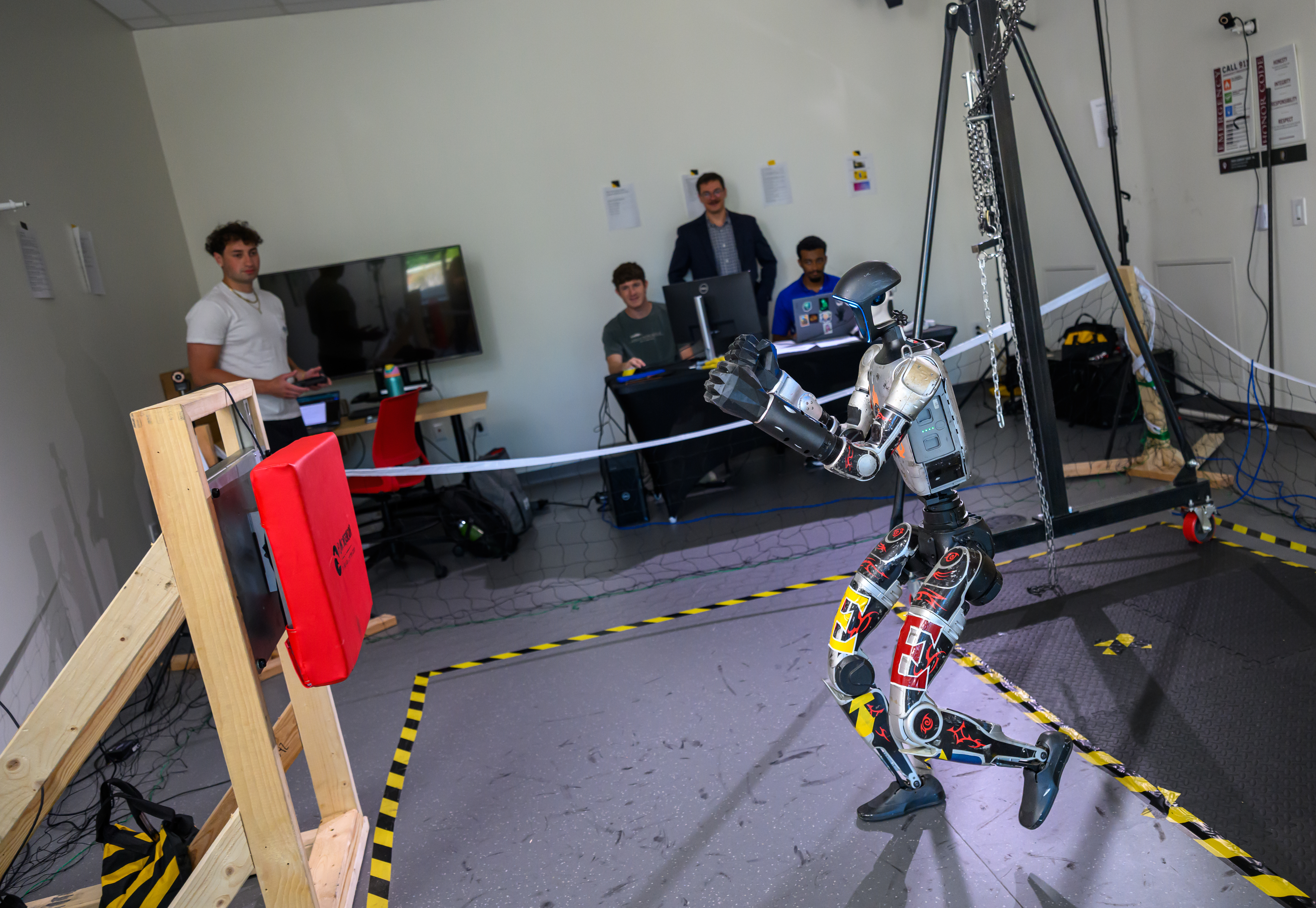 A humanoid robot moves inside a research lab as students and faculty watch from behind a rope.
