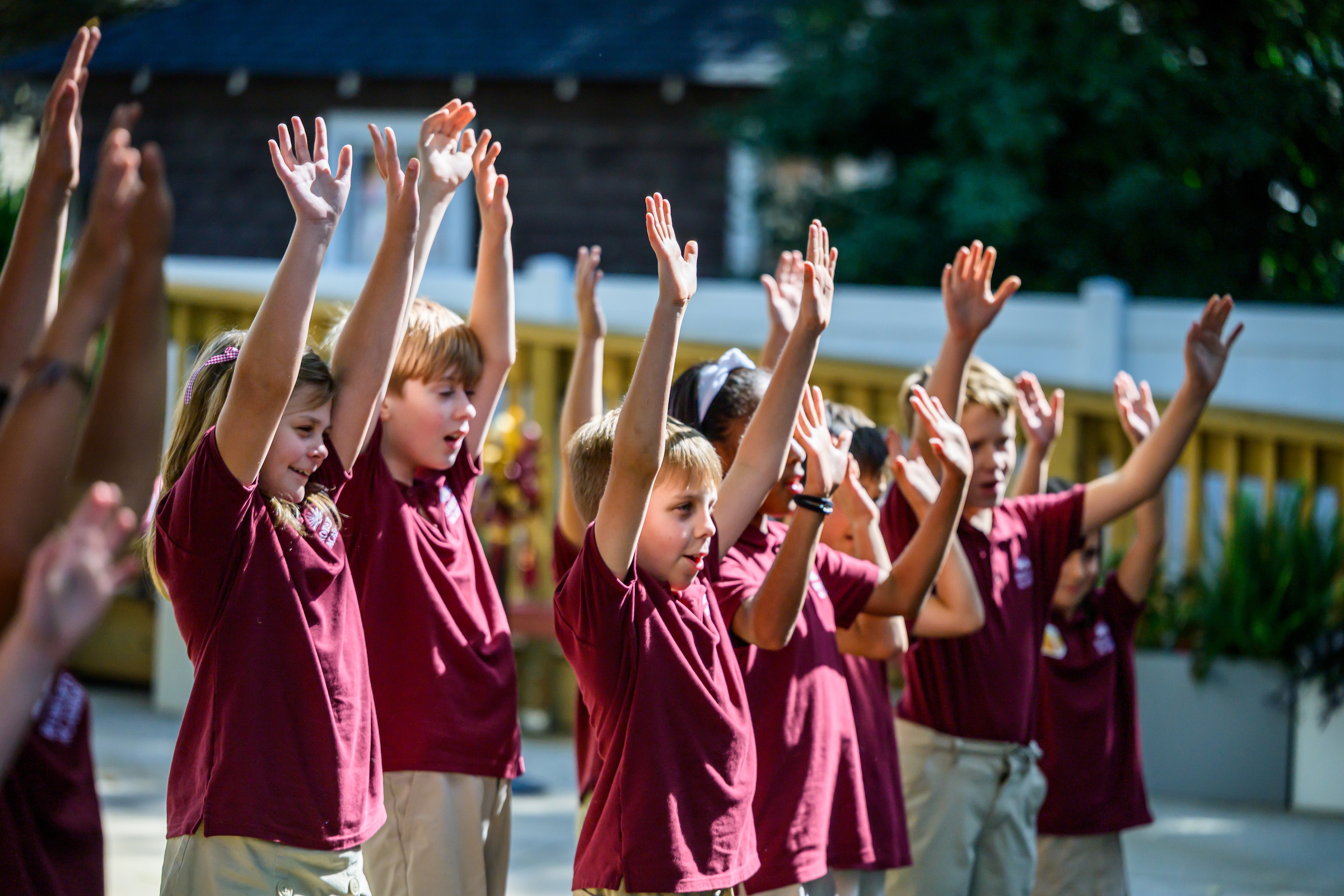 A photo of children wearing maroon shirts with their hands in the air as they perform a cheer for those in attendance at a ribbon-cutting for the Roberts Academy at Elon University.