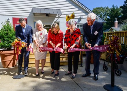 A photo of five people cutting a maroon ribbon in front of the entrance to an elementary school on the campus of Elon University.