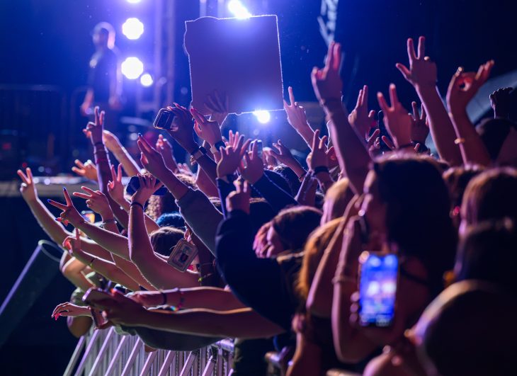 Concertgoers raise their hands and phones toward the stage under bright blue and purple lights during Elon’s Rock the Block concert.
